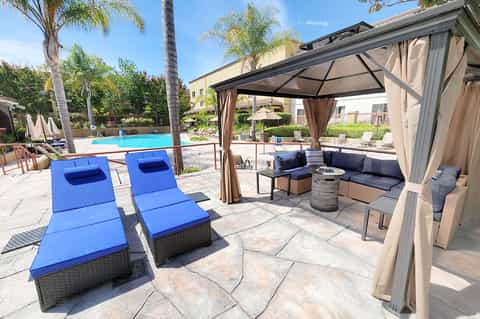 Resort pool deck with blue lounge chairs, pergola shade structure, and palm trees