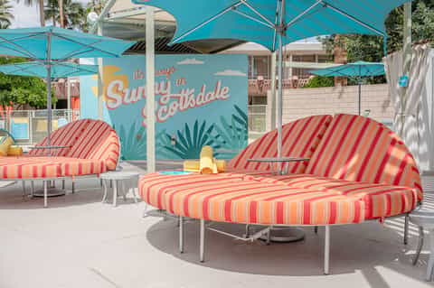 Colorful striped loungers under turquoise umbrellas in a sunny poolside area with palm trees
