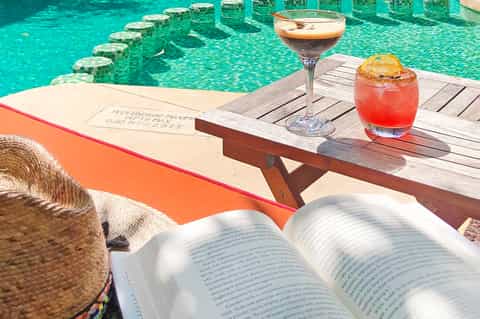 Tropical cocktails on wooden deck overlooking turquoise infinity pool