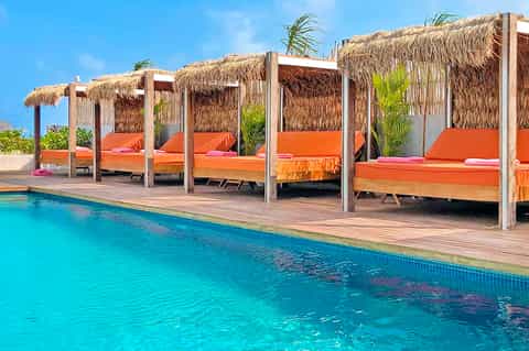 Resort poolside cabanas with orange cushions, thatched roofs, and turquoise water