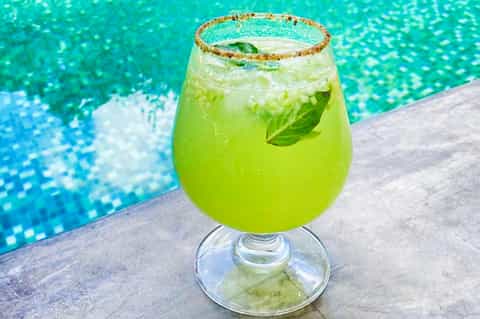 Bright green cocktail with salt rim and mint leaf by turquoise swimming pool