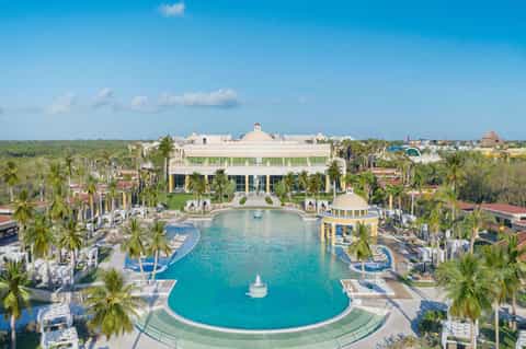 Aerial view of resort with curved turquoise pool, palm-lined grounds, and main building
