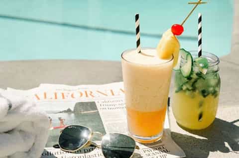 Two tropical cocktails poolside with newspaper and sunglasses on a sunny day