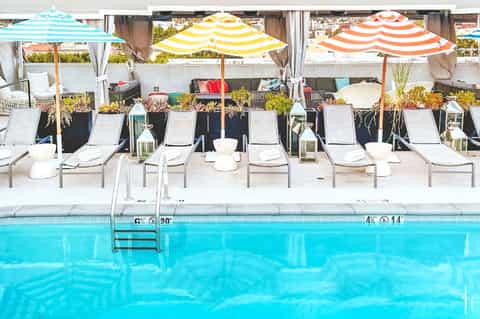 Resort pool deck with colorful striped umbrellas, lounge chairs, planters, and blue pool water