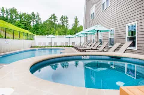 Residential pool area with hot tub, lounge chairs, and green umbrellas by house