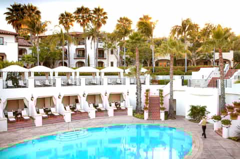 Resort pool surrounded by white cabanas, palm trees, and Mediterranean-style buildings