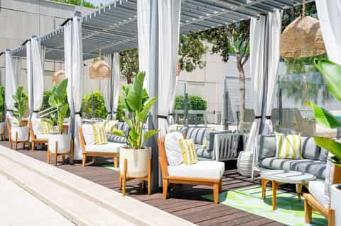 Upscale patio lounge with wooden pergola, woven pendant lights, and striped cushioned seating