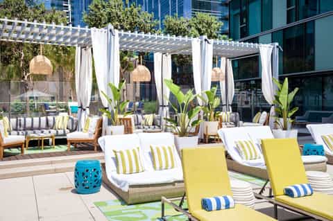 Upscale rooftop lounge with pergola, white cabanas, yellow loungers, and tropical plants