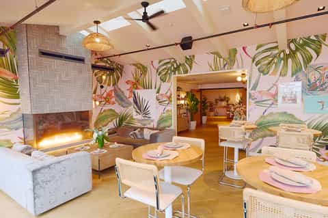 Modern dining room with tropical botanical wallpaper, fireplace, natural lighting, and round wooden tables