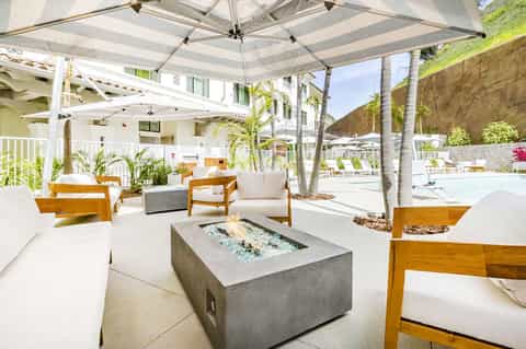 Modern resort lounge area with fire pit, wooden chairs, and striped umbrellas