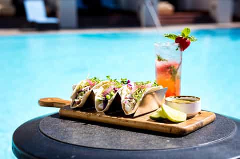 Gourmet fish tacos with colorful salad and cocktail displayed poolside