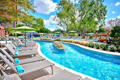 Bright outdoor pool with lounge chairs, green umbrellas, and lush landscaping under blue sky