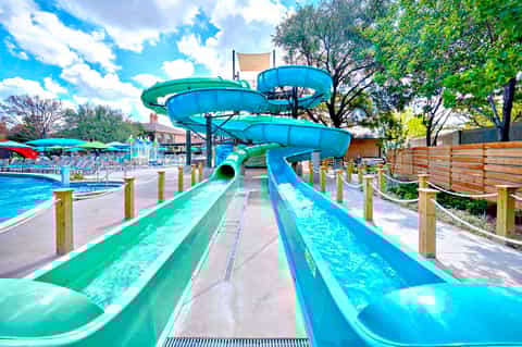 Water slides at outdoor pool complex with blue slides, clear sky, and surrounding trees
