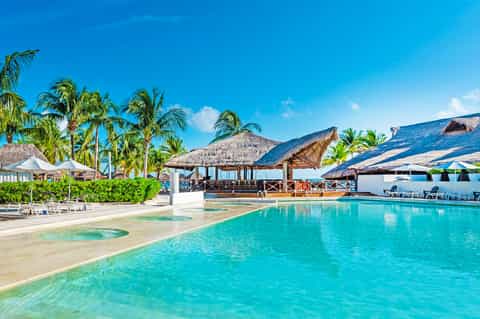 Luxury tropical resort pool with thatched-roof bungalows, white loungers, palm trees, and crystal-clear turquoise water