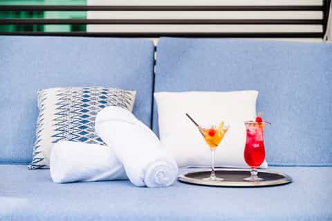 Blue upholstered sofa with white pillows, rolled towels, and colorful cocktails on side table