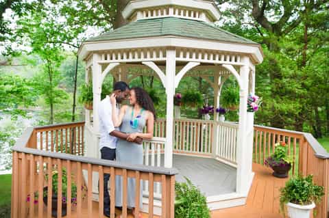 Couple embracing in a white gazebo surrounded by flowers and forest scenery