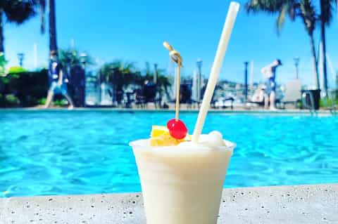 Tropical cocktail with cherry garnish by poolside with palm trees and city skyline in background