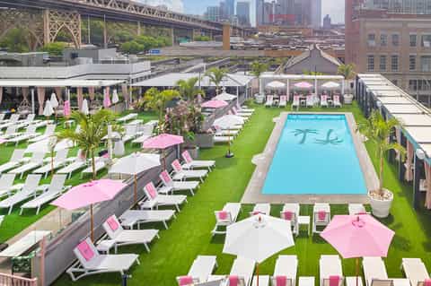 Rooftop pool deck with pink and white umbrellas, lounge chairs, and city skyline with bridge view