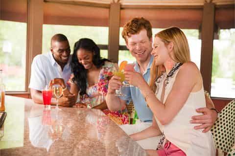 Four guests toasting with tropical cocktails at resort bar near windows