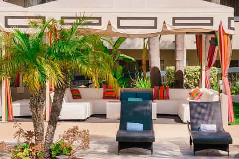 Outdoor lounge area with white modular seating, palm tree, colorful fabric drapes and pergola shade