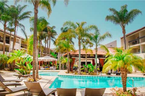 Mediterranean-style resort courtyard with turquoise pool, palm trees, lounge chairs, and Spanish architecture