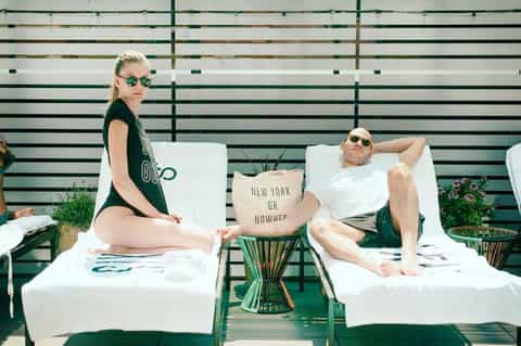 Two guests relaxing on white lounge chairs against a striped green and white backdrop