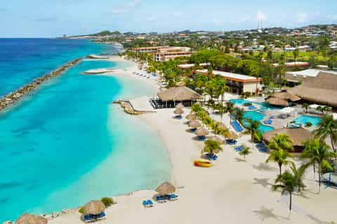 Aerial view of tropical beachfront resort with turquoise lagoon, thatched-roof huts, and palm trees