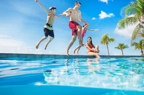 Family jumping into resort pool with palm trees and blue sky in background