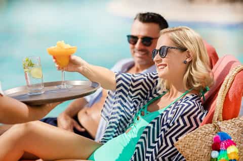 Couple enjoying tropical drinks and appetizers by the pool in resort attire