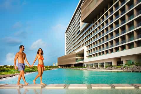 Couple walking along turquoise pool at modern beachfront resort with high-rise hotel building