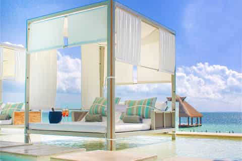 Luxury beachfront cabana bed with white curtains overlooking turquoise ocean