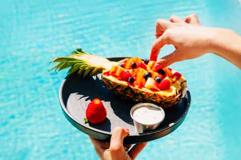 Poolside fruit platter with decorated pineapple, berries, and whipped cream