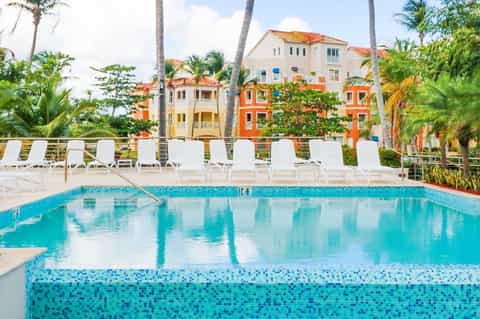 Resort pool with white lounge chairs, colorful buildings, and palm trees