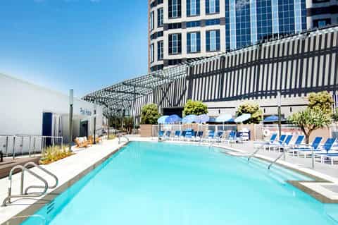 Resort swimming pool with blue lounge chairs, pergola shade structures, and high-rise building