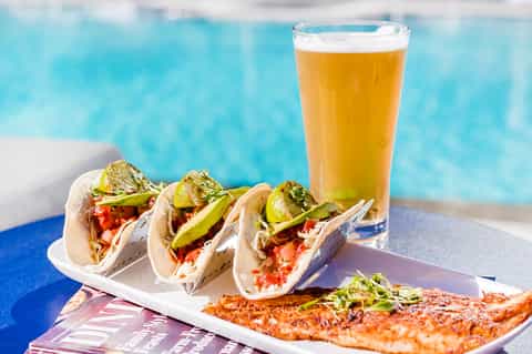Poolside snack with fish tacos, lime garnish, and beer overlooking turquoise pool water