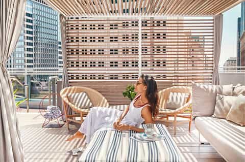 Woman relaxing on sunny rooftop terrace with striped shade screen and city views