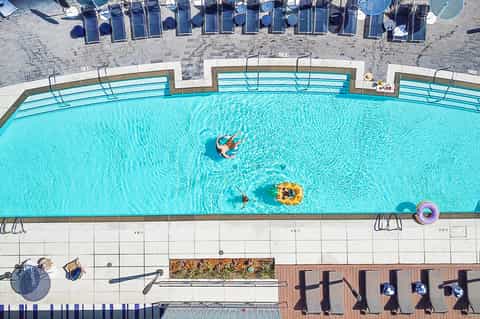 Aerial view of resort swimming pool with guests on floats, lounge chairs, and sunny poolside area