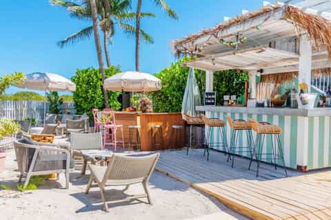 Beach bar with thatched roof, umbrellas, and palm trees on sandy shore