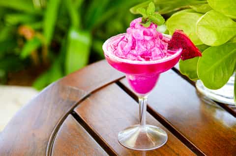 Vibrant pink frozen margarita cocktail with salt rim, garnished with lime and surrounded by foliage