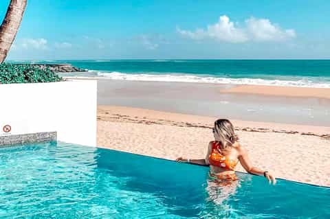 Woman in infinity pool overlooking tropical beach with turquoise ocean and white sand