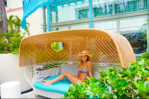 Woman in swimwear reclining in modern woven daybed with turquoise cushion