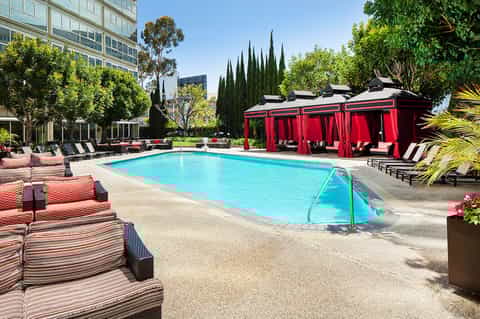 Modern urban resort pool surrounded by lounge seating and distinctive red cabana pavilions