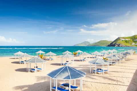 Sandy beach lined with white cabanas and blue loungers overlooking turquoise ocean and green islands