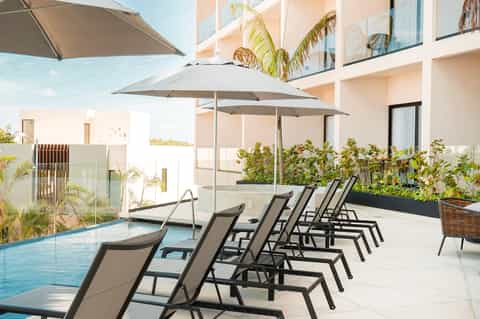 Resort poolside with gray umbrellas, black lounge chairs, and modern building with palm trees