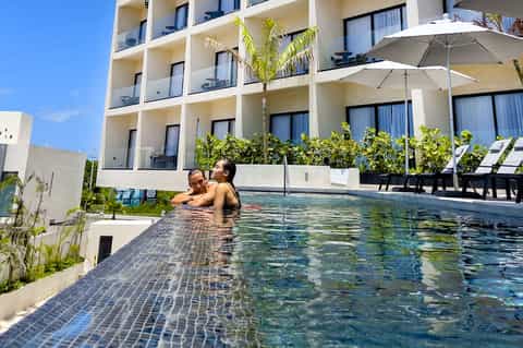 Couple swimming in resort infinity pool with modern building and white umbrellas
