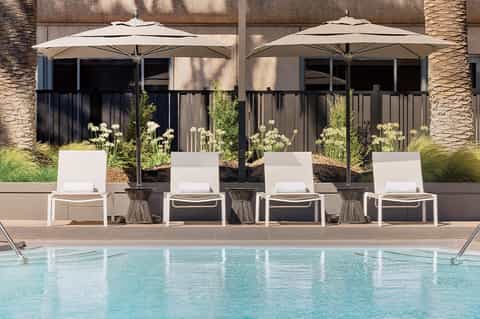 Poolside lounge chairs under large white umbrellas with landscaped planters and stone terrace