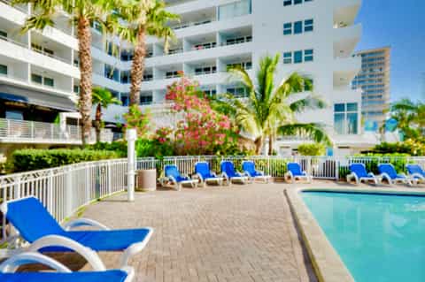 Resort pool deck with blue lounge chairs, palm trees, and multi-story white hotel building
