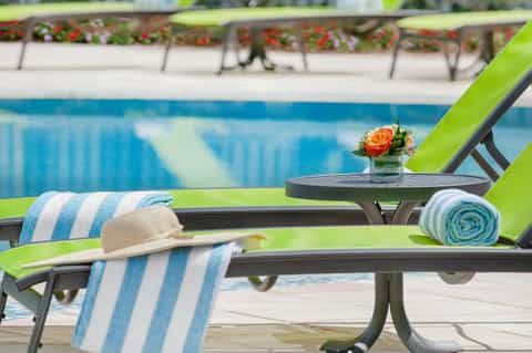 Pool-side lounge chair with striped towel, small table with flower arrangement, and blue pool water in background