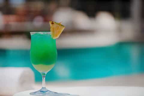 Green tropical cocktail with pineapple slice at poolside bar