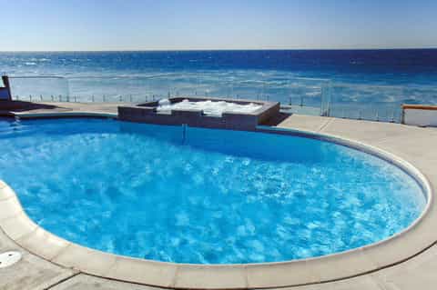 Curved resort pool with ocean view, spa area, and clear blue sky